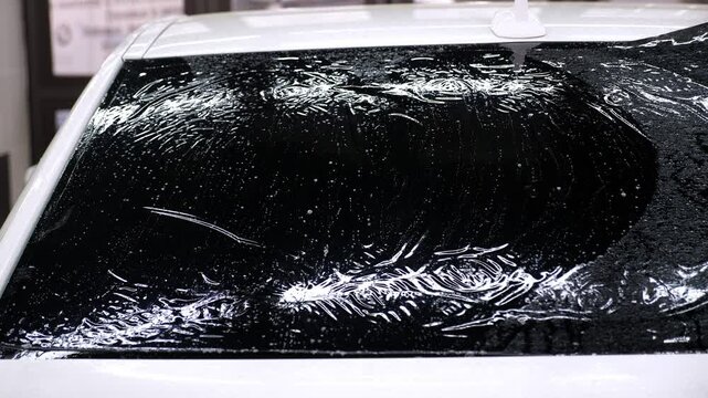A close-up of a car service master splashing water on the glass before gluing tinted film in an auto repair shop. The process of tinting the car.