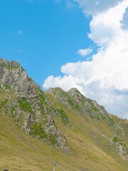 Rocky mountain terrain features lush greenery and a clear blue sky with scattered clouds