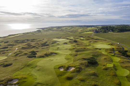 Aerial view of the Castle Course's undulating greens meeting the sea under a soft sky, St Andrews, Scotland, United Kingdom.