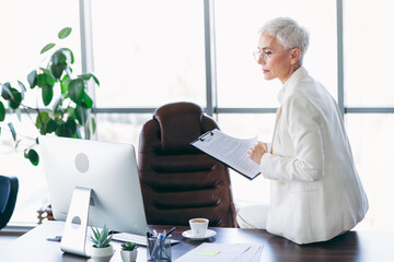 Professional senior businesswoman reviewing documents in a modern office workspace with natural...