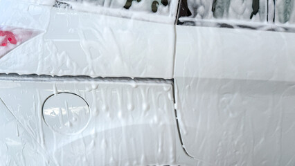 Suds cling to white car body, a frothy embrace reminiscent of Bubble Bath Day, cleansing ritual...