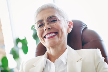 Confident senior businesswoman sitting in a modern office chair and smiling confidently wearing...