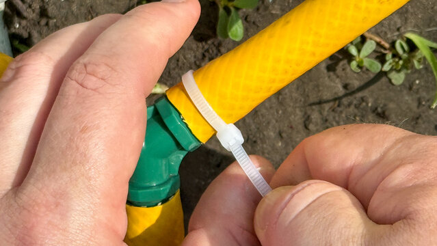 Ingenious hands of a Caucasian male fastening a garden hose for World Plumbing Day and the quirky art of ziptie crafts