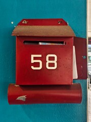 Red Wall-Mounted Mailbox with Numbering Against Teal Background