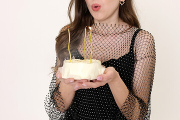 Holding a cake in her hands, a girl blows out the candles. Birthday celebration.