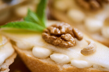 Toasted bread with creamy spread, pear slices, and walnuts makes a delightful appetizer for any gathering.