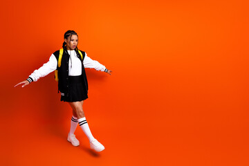 Teen girl in fashionable jacket and skirt posing on orange backdrop emphasizing education, style,...