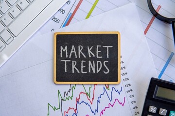 A small blackboard with word "MARKET TRENDS" placed on a colorful line graph. Financial analysis, business intelligence, and economic forecasting concept.