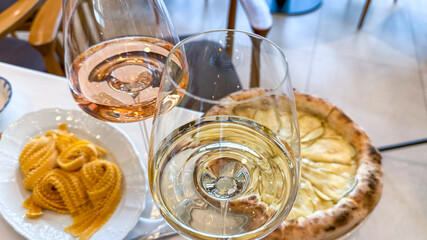 Two glasses of rose and white wine sparkle beside rustic pasta and tantalizing pizza, evoking La Dolce Vita celebration