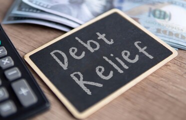 A blackboard with "Debt Relief" written in chalk, a calculator and US dollar bills. Financial solutions, managing debt concept.