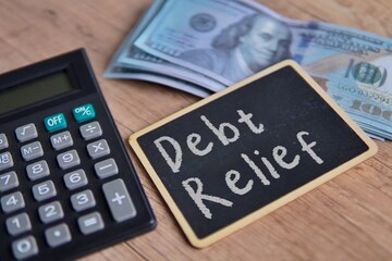 A blackboard with "Debt Relief" written in chalk, a calculator and US dollar bills. Financial solutions, managing debt concept.