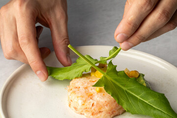 Two hands artfully garnish salmon tartare with wild leaves, evoking a culinary ritual for Midsummer...