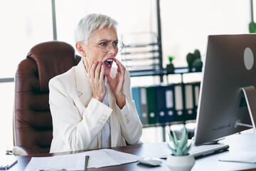 Elegant senior businesswoman expressing surprise while working in a professional office environment...