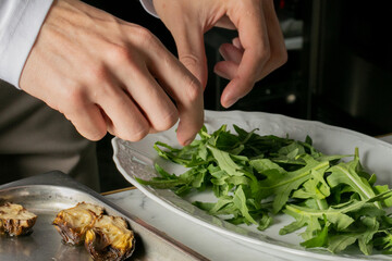 Crafting a savory salad symphony, a Caucasian male elegantly garnishes arugula, echoing Earth Day's nod to mindful culinary artistry