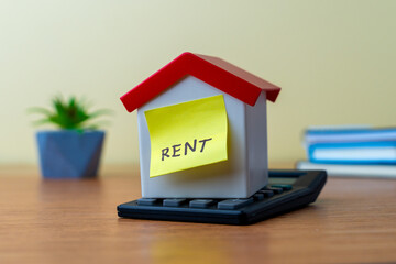 A miniature house on top of a calculator and a yellow sticky note with the word 