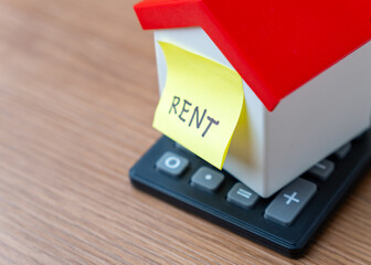 A miniature house on top of a calculator and a yellow sticky note with the word 
