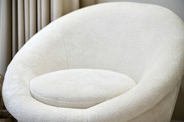 A modern round white chair sits elegantly in a softly lit living space with curtains in the background.