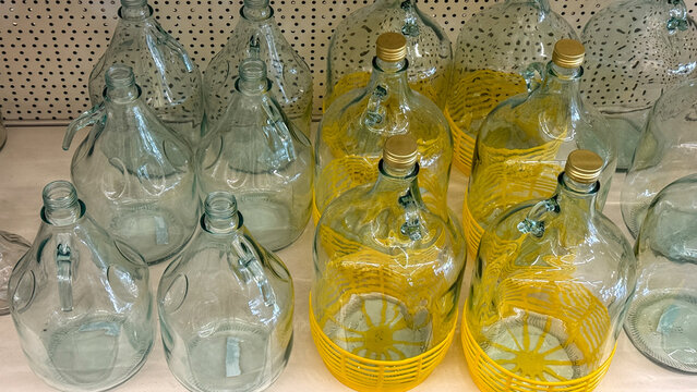 Transparent glass demijohns with whimsical yellow accents evoke harvest festivities, upcycling creativity, and local cider-making traditions