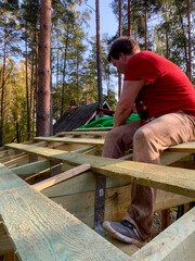 A Caucasian man in a vibrant red shirt builds dreamlike forest cabin, capturing rustic nostalgia, Arbor Day spirit