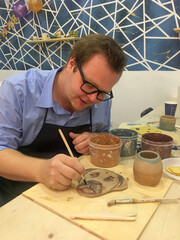 A Caucasian man immersed in ceramic artistry, painting earthenware like an ancient craftsman during World Art Day celebrations