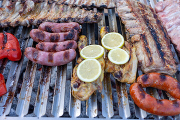 Sausages, chicken with lemon and pork ribs grilling on barbecue