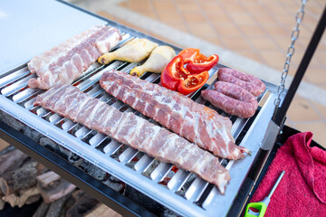 Chef grilling ribs, chicken legs, sausages and red bell peppers for summer barbecue party