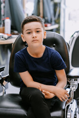 A patient boy sits still while a stylist carefully trims his hair, surrounded by the creative patterns of the salon.