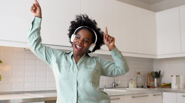 Confident carefree african american woman dancing in kitchen wearing headphones sings along to favorite song enjoys single life. Self love of contented black female spending weekend with music at home