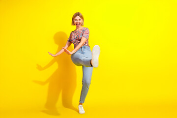 Cheerful young woman posing energetically in a stylish outfit against a vibrant yellow background
