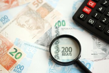 Brazilian reais banknotes and calculator with magnifying glass. Brazil real money, calc with loupe