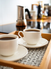 Two white cups with black coffee standing on tray on kitchen table, close-up