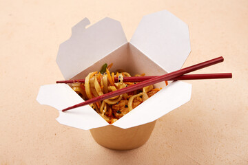 Noodles served in takeout box with chopsticks on a simple background