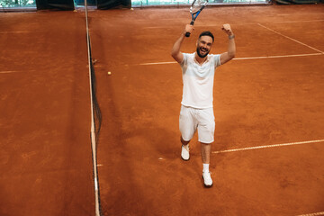 Celebrating victory, happy face. Man is playing tennis indoors in the hangar