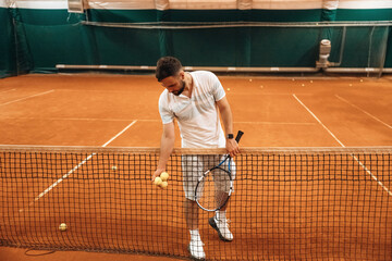 Obraz premium In white sport clothes. Man is playing tennis indoors in the hangar