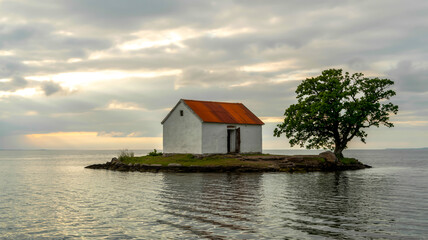 Obraz premium A minimalist landscape photo of a white house with red-orange roof, isolated on a tiny island, surrounded by calm waters