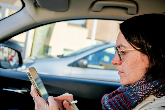 Woman in a car using a smartphone, wearing glasses and a scarf on a sunny day. Burgundy, France