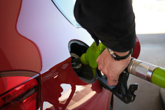Hand refueling a red car at a gas station with a green fuel nozzle. Burgundy, France