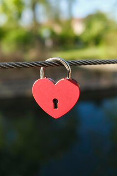 Red heart-shaped padlock hanging on a metal cable over blurred background. Vosges, Alsace, France