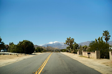 Desert road leading to distant snow-capped mountains under a clear blue sky. Mojave Desert, USA