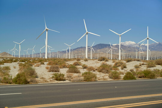A row of wind turbines in a desert landscape with mountains and clear blue sky. Mojave Desert, USA