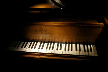Close-up of a wooden piano keyboard in dim, dramatic lighting.