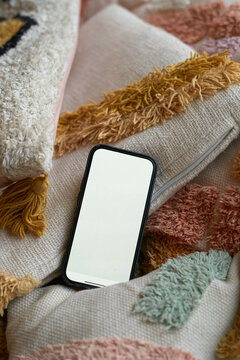 A smartphone with a blank screen rests on colorful textured pillows.