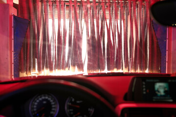 Interior view of a car entering an automated car wash with vibrant red lighting.