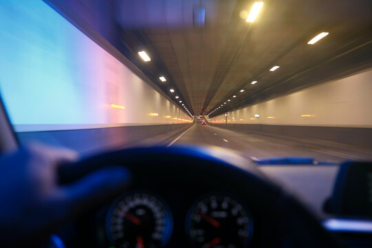 Blurred view from inside a moving car driving through a brightly lit tunnel.