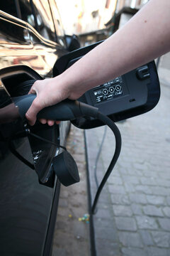 Hand plugging in an electric car charger on a street with cobblestone pavement.