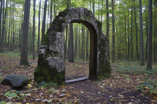 Mysterious stone gateway stands in a serene forest surrounded by tall trees on an overcast day