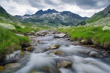 Majestic alpine mountain landscape with clear river stream flowing over rocks and green meadows under blue sky
