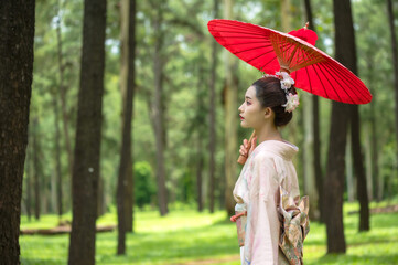 Beauty young Japanese woman dressing in traditional kimono or yukata holding red umbrella walking...
