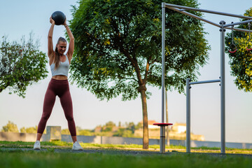 Concentrated sportswoman performing an overhead medicine ball lift during her workout in a...