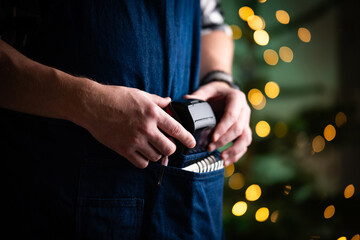 Waiter Takes The Wireless Pos Terminal From Pocket In A Restaurant At Christmas